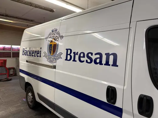 Ein weißer Lieferwagen mit der Aufschrift „Bäckerei Bresan“ und einem Wappen fährt in einer Garage oder Halle
