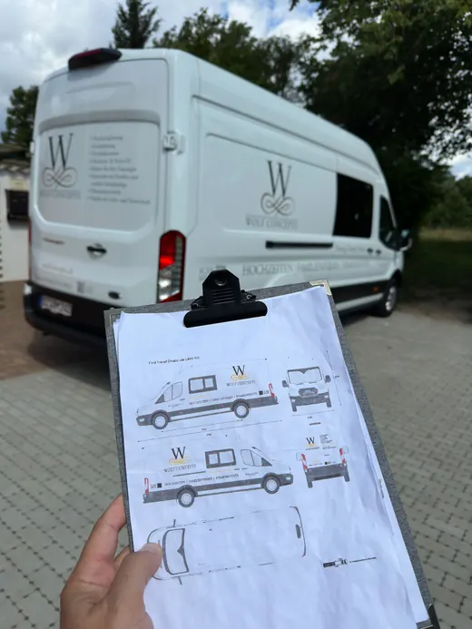 Eine Person hält einen Klemmbrett mit Designplänen für die Fahrzeugbeschriftung vor einem weißem Lieferwagen, der bereits das gleiche Design trägt