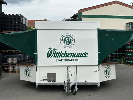 Ein mobiler Bierstand mit Wittichenauer Stadtbrauerei Logo, grün-weiße Farben, Anhänger auf einem Hof, sichtbar von hinten, ANKERHELD Ausstattung. © Kellermanns