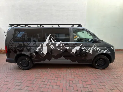 Schwarzer Van mit schwarzer und weißer Berglandschaft-Grafik an der Seite, geparkt auf einem roten Pflastersteinboden vor einer hellen Wand