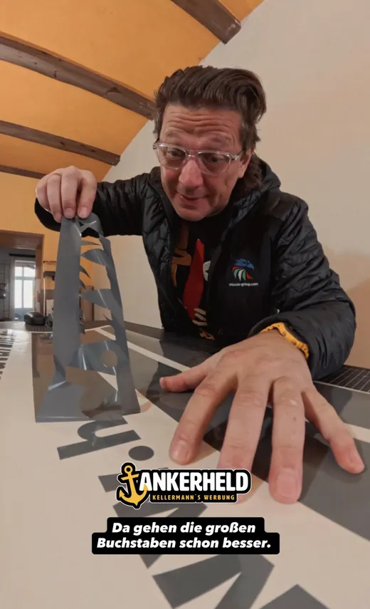 Ein Mann mit Brille betrachtet ein kleines, graues Modell auf einem Tisch. Im Vordergrund ist seine Hand, unten steht „ANKERHELD“