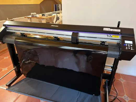 Großer Drucker druckt schwarzes Material auf einer Rolle in einem Innenraum mit gelb-beigen Wänden im Hintergrund