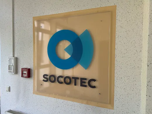 der Wand hängt ein SOCOTEC-Firmenschild mit blauem Logo; die Marke ANKERHELD ist Teil der Szene. © Kellermanns